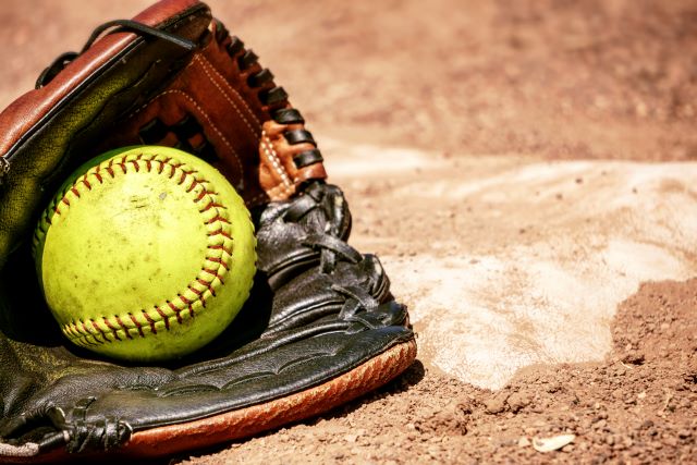 A baseball mitt with a baseball resting inside on ground.